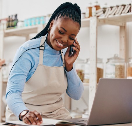 A woman laughing on the phone while she works on her laptop